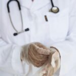 Faceless ethnic medical worker in lab coat and stethoscope taking of transparent gloves after approaching patients for examination in modern hospital