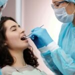 Dentist in protective gear examining a woman's teeth during a dental clinic visit.